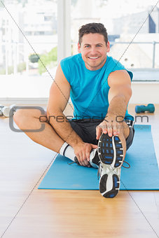 Sporty man stretching hand to leg in fitness studio