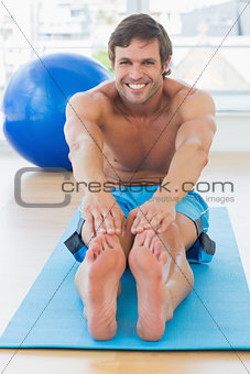 Sporty man stretching hands to legs in fitness studio