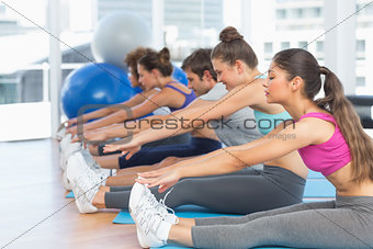 Sporty people stretching hands to legs in fitness studio