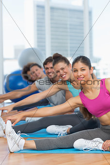 Sporty people stretching hands to legs in fitness studio