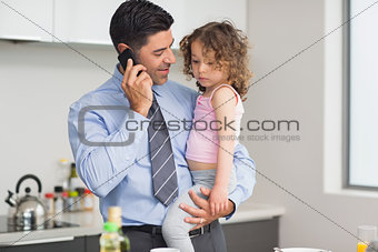 Well dressed father carrying daughter while on call in kitchen