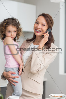 Well dressed mother carrying daughter while on call in kitchen