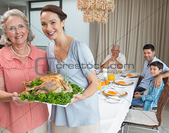 Woman and grandmother holding chicken roast with family at dining table