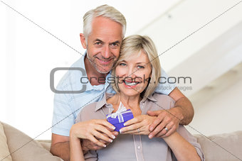 Smiling mature man surprising woman with a gift on sofa