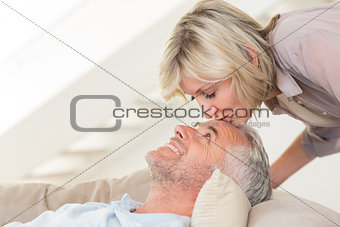 Side view of a woman kissing a relaxed mature mans forehead in the living room at home