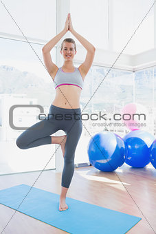 Smiling woman standing in tree pose at gym