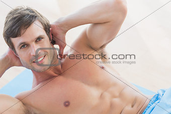 Portrait of a smiling shirtless young man doing sit ups