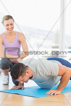 Smiling trainer assisting man with push ups