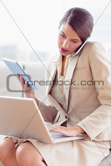 Busy businesswoman sitting on sofa multi tasking