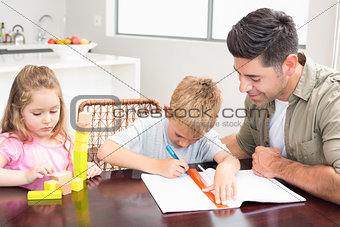 Father helping son with homework with little girl playing with blocks