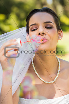 Beautiful bride blowing soap bubbles in park