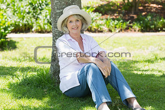 Mature woman sitting against a tree in park