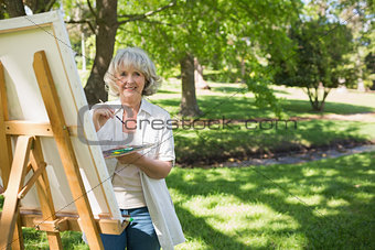 Smiling mature woman painting in park