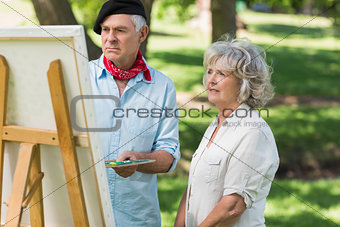 Woman watching mature man paint in park