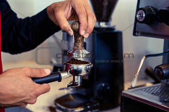 Barista pressing fresh coffee grounds
