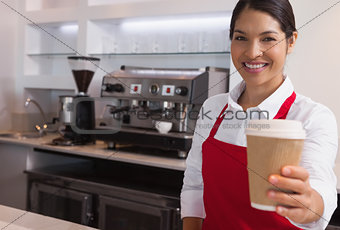Happy young barista offering cup of coffee to go smiling at camera