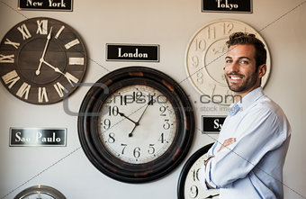 Happy businessman standing beside wall of international clocks