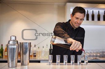 Happy bartender pouring cocktail into shot glasses