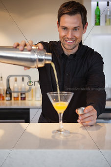 Smiling bartender pouring cocktail into glass