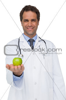 Happy doctor smiling and holding apple to camera