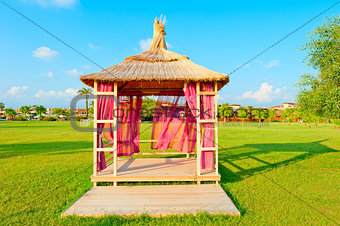 gazebo with a thatched roof on a green lawn