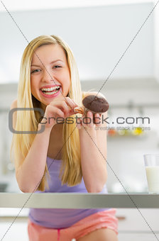 Happy young woman eating chocolate muffin in kitchen