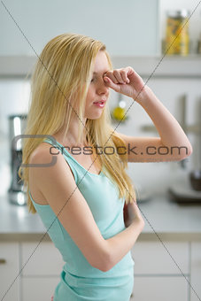 Young woman rubbing eyes after sleep in kitchen