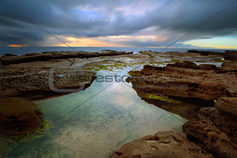 Stormy sunrise over Little Bay with rockpool in foreground