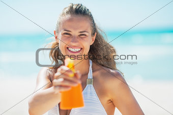 Smiling young woman pointing bottle of sun block creme in camera