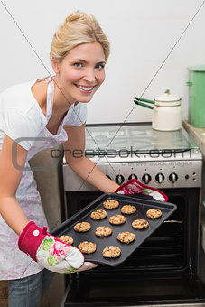 Smiling woman putting a tray of cookies in oven