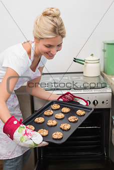 Smiling woman removing a tray of cookies from the oven