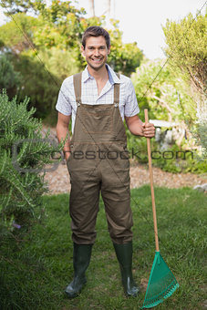Young man in dungarees holding rake in garden