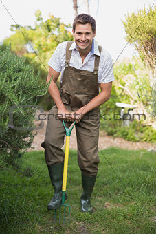Happy man in dungarees raking the garden