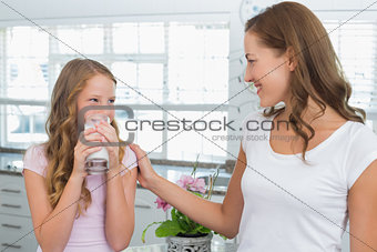 Girl drinking milk as she looks to her mother in kitchen