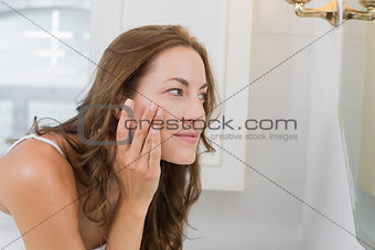 Side view of a beautiful young woman examining her face