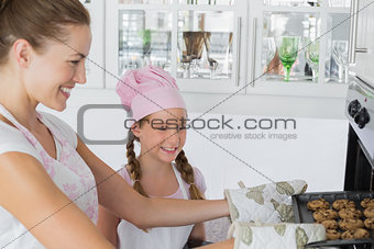 Girl looking at mother remove cookies from oven