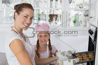 Girl with mother removing cookies from the oven