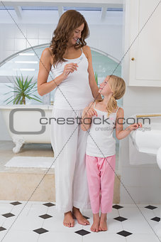 Girl brushing teeth as she looks at her mother in bathroom