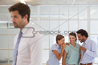 Colleagues gossiping with sad businessman in foreground