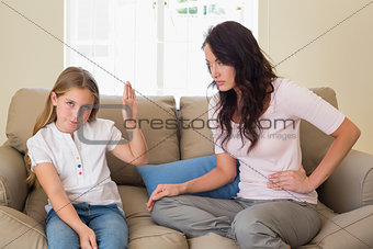 Girl showing stop gesture to mother on sofa