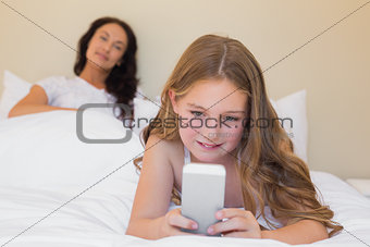 Girl using mobilephone on bed with mother in background