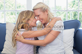 Mother and daughter rubbing noses on sofa
