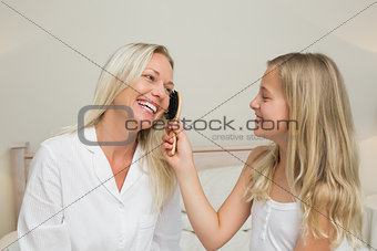 Girl brushing hair of mother in bedroom