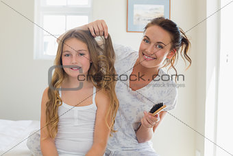 Mother making hair of daughter in bedroom