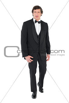 Groom in tuxedo walking over white background