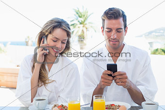 Couple using mobile phones while having breakfast