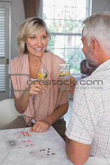 Mature couple toasting drinks while playing cards at home
