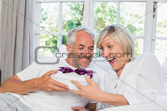Mature man giving surprised woman gift box at home