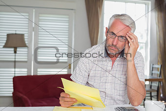 Serious mature man sitting with home bills