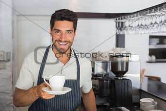 Smiling male barista holding cup of coffee at café